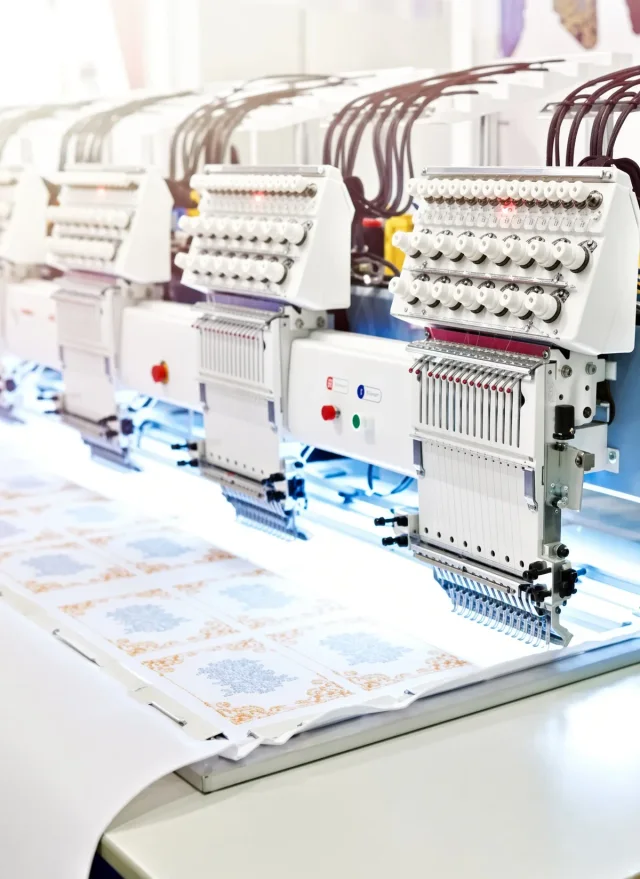 Multi-head embroidery machine stitching an emblem across a row of garments