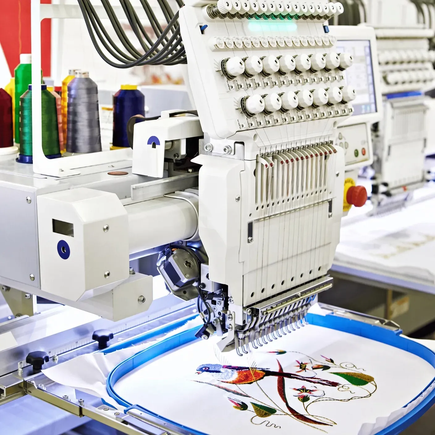 Multi-head embroidery machine with colour-change thread rails stitching a logo in production